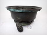 une image représentant un petit pot en bronze posé sur une surface blanche