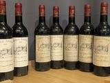 six bottles of red wine are lined up on a wooden barrel