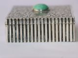 silver box with a green stone on top of it on a white surface