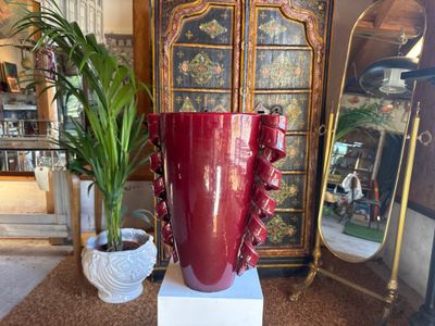 a large red vase sitting on a pedestal next to a potted plant
