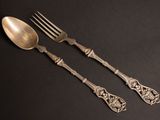 two silver spoons and a fork on a black surface