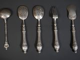 five silver spoons and a fork are lined up on a black surface