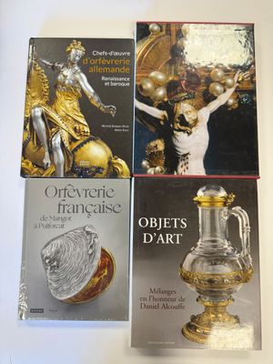trois livres posés sur une table blanche, accompagnés d'un vase doré et d'autres objets