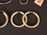 three pairs of gold hoop earrings and a pair of scissors on a black surface