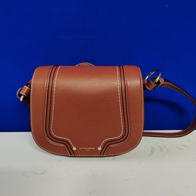 a brown leather cross body bag on a white table
