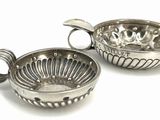two silver metal bowls with handles on a white surface