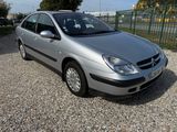 the silver car is parked in a gravel lot near a fence