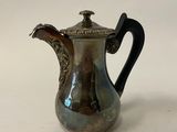 an antique silver coffee pot with a black handle on a white surface
