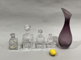 a purple glass vase, a bottle, and a banana on a white surface