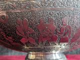 a silver bowl with a design on it on a red cloth