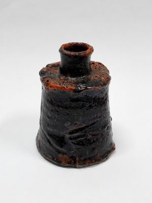 un petit vase noir au couvercle rouillé, posé sur une surface blanche