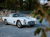 une voiture de collection blanche garée devant un mur de pierre