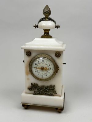 une petite horloge blanche surmontée d'un oiseau