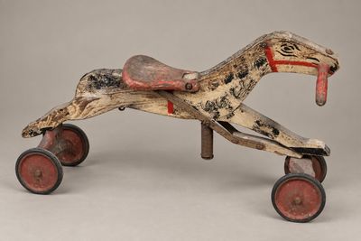 un cheval jouet en bois à l'ancienne, muni de roues, sur fond gris