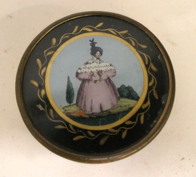 une petite boîte noire et dorée sur laquelle figure l'image d'une femme en robe rose