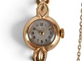une montre en or entourée d'une chaîne sur une surface blanche