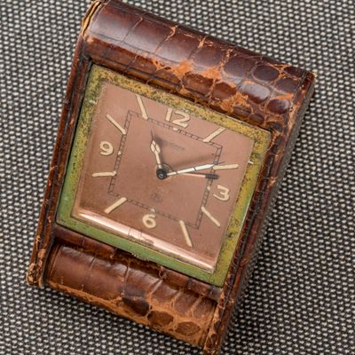 une image représentant une montre carrée marron et verte posée sur une surface grise