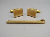 two gold cufflinks and a tie bar on a table
