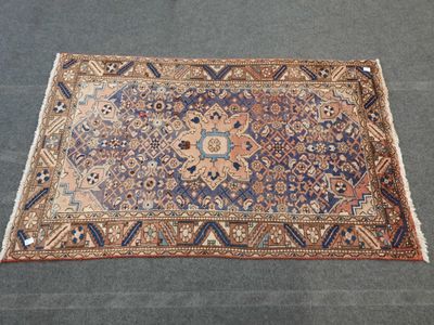 un tapis persan ancien aux motifs bleus et orange posé sur un sol gris