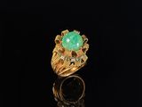 a gold ring with a green stone and diamonds on a black surface
