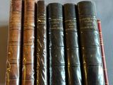 six old books are lined up on a white surface