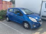 a small blue car parked in a parking lot next to a truck