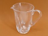 a clear glass pitcher with a handle on a brown surface