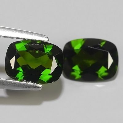 pair of green tourmaline gems on a white surface with a pair of tongs