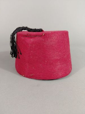 chapeau en feutre rose orné d'un pompon noir sur fond blanc