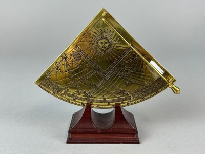 un cadran solaire en laiton posé sur un socle en bois, sur fond blanc