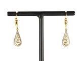 une paire de boucles d'oreilles en or et diamants posée sur un socle noir