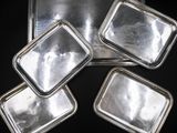 quatre plateaux en argent avec couvercles, posés sur une surface noire