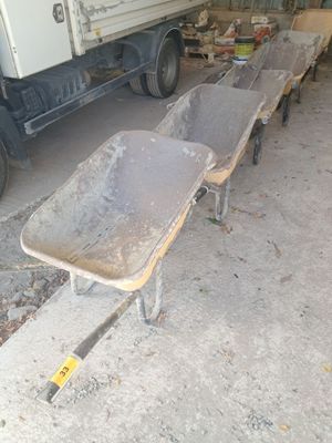 Plusieurs brouettes sont alignées dans un garage, avec un camion en arrière-plan.