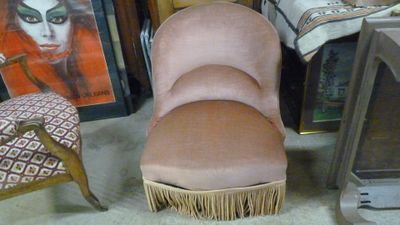 une chaise rose ornée de franges, placée devant des tableaux