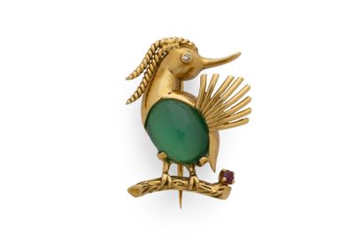 une image représentant une broche en forme d'oiseau doré et vert posée sur une branche