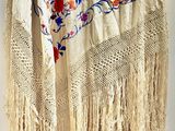 a white shawl with flowers and fringes on a mannequin