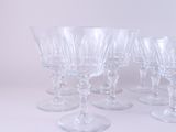 six clear wine glasses are lined up on a white surface