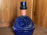 une bouteille en verre bleue ornée d'un pentagramme, posée sur une étagère en bois