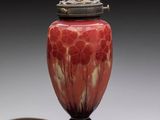 a red and white vase with a metal lid on a table