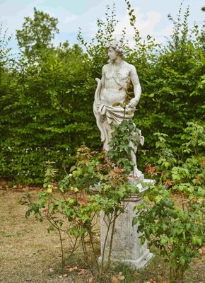 une statue représentant un homme assis sur un socle au milieu d'un jardin