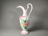 un vase blanc muni d'une anse rose et orné d'un motif floral