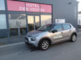 une voiture grise garée devant un immeuble, sur le côté de laquelle est accrochée une pancarte