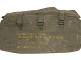 un vieux sac militaire sur lequel est inscrit un message, posé sur une surface blanche