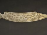 a silver knife with a plaque on it sitting on a black surface