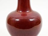 un vase rouge posé sur une surface blanche