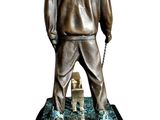 statue of a man in a hoodie standing on a rock with a boat in the water