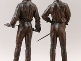 pair of bronze figurines of a man and a woman holding a sword