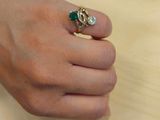 a woman ' s hand holding a green and white diamond ring