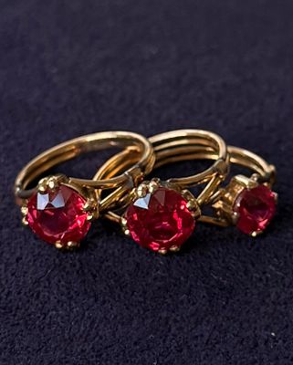 three gold rings with red stones sitting on a black surface