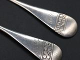 two silver spoons with designs on them on a black surface